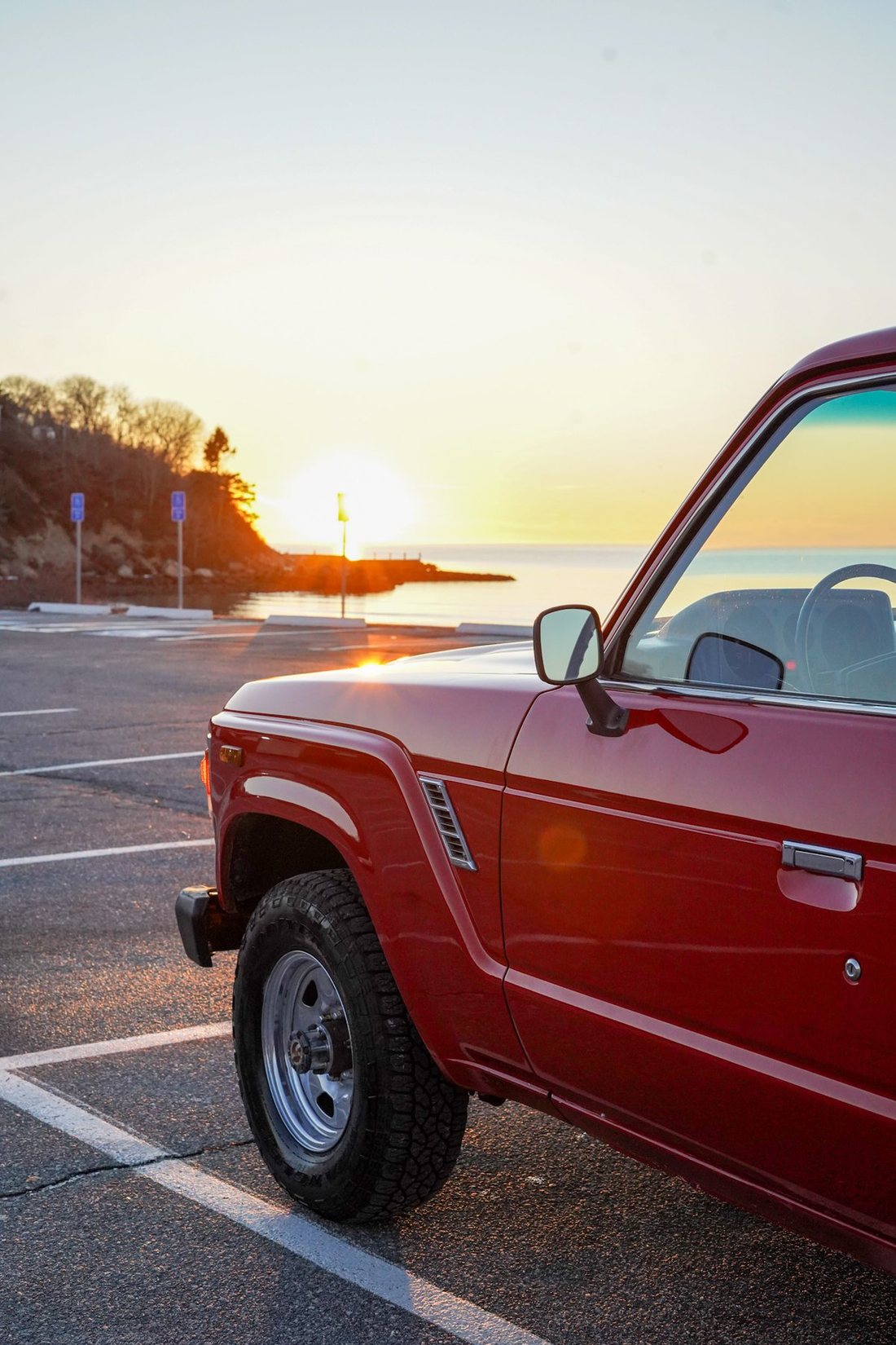 Red Land Cruiser FJ60 at sunrise beside the water